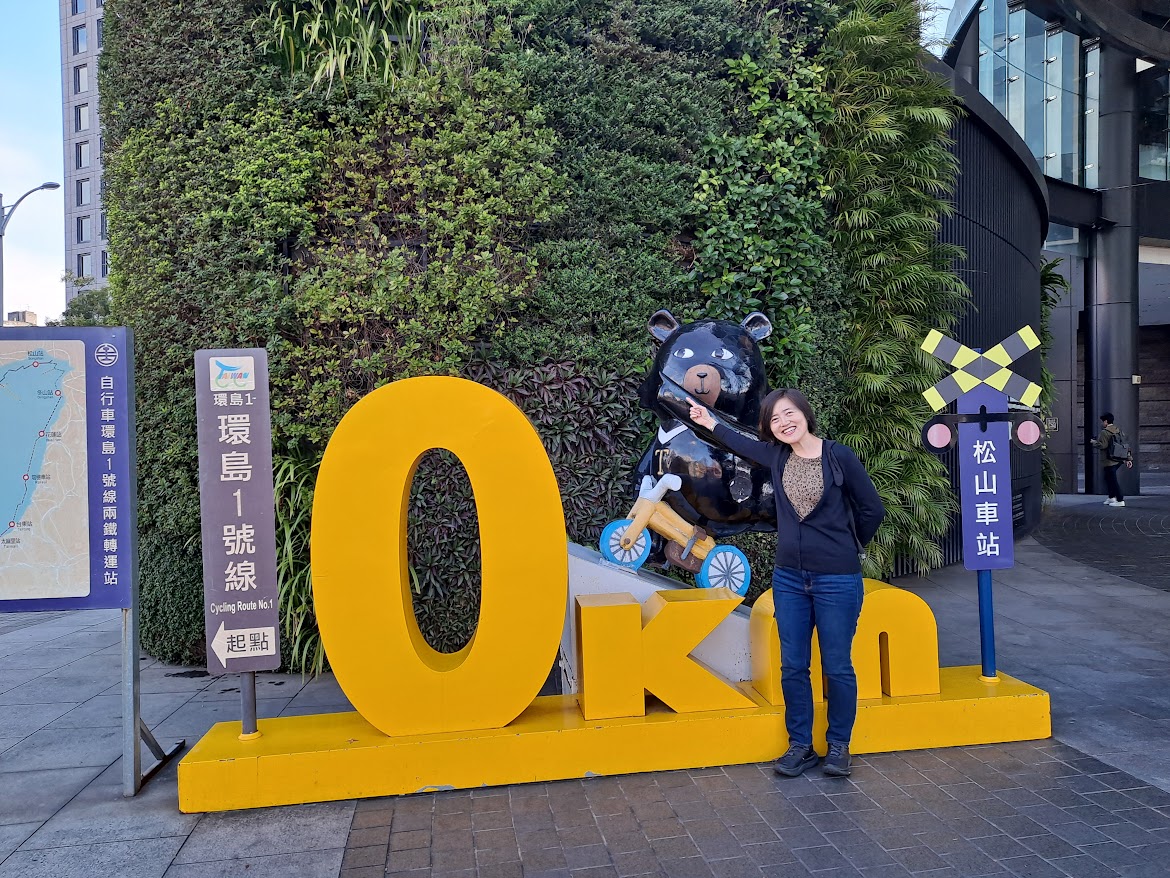 Yurika Kurakata standing next to a sign with a bear on a bicycle in Taiwan.