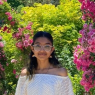 Picture of Shivaangi smiling at the camera, with shoulder-length black hair, glasses, and a white shirt.