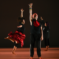 three dancers in red and black raise one arm above their head