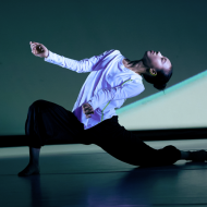 a dancer in a white shirt and black pants in a deep lunge with head arched back.
