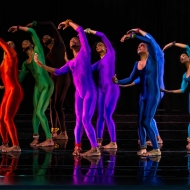 From Before (1978) by Garth Fagan photo by John Schlia. Several dancers in bright colored unitards raise their arms in a circle bent to the side.