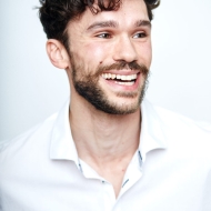 Yuri Fortini, Accademia Dell Arte, Italy dance teacher in a white shirt, curly hair and a beard with a big smile.