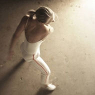 Dancer in a white leotard, pants, and shoes with blonde hair seen from above looks to the right. Photo, Tori Lawrence