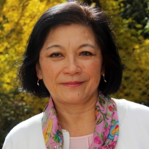 A woman with black hair, white sweater, and pink floral scarf.
