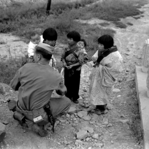 A group of three Japanese children talking to an uniformed U.S. soldier.