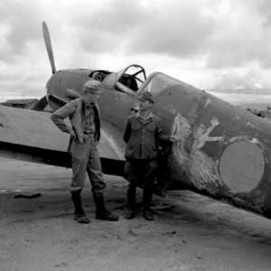 Two soldiers standing in front of a military airplane.