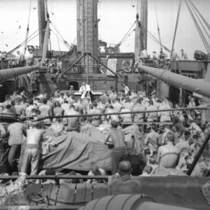A large group of shirtless men, with their backs to the camera, on a battleship during World War Two.