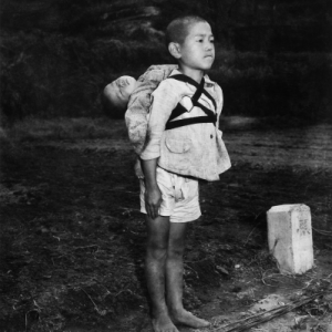 A boy carrying a baby stands erect at a cremation site.