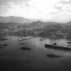 A harbor in Japan full of military ships with mountains in the background.
