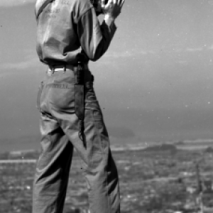 A man standing on top of a building taking a photograph of the city below him.