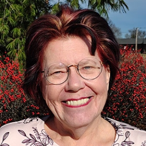 Portrait of Cathy Hews outside with winter berry bushes and evergreens in the background