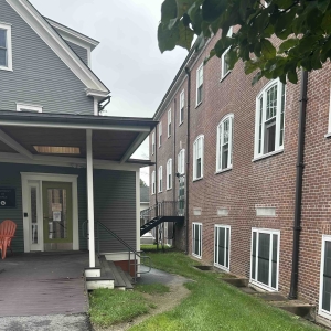 An alleyway with a black staircase between a gray house and a brick building
