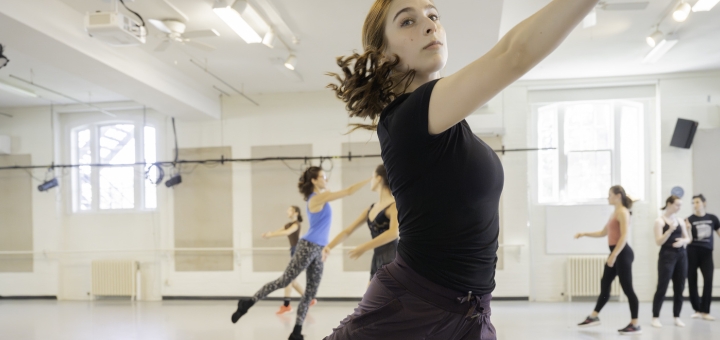 A dancer in black sautees across a white studio. Photo by nikki lee.
